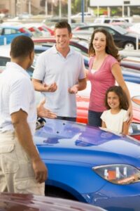 Family discussing new car with salesman on lot